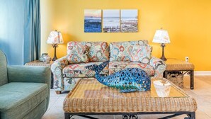 A living room with a sofa, two side tables, a coffee table, and a wall with three paintings. - Cozy Gulf Front Condo With Beach Front View | Beach Access | Pool | Sleeps 6 (Gulf Shores)