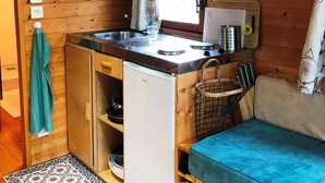 Cocina compacta con paredes de madera, microondas, un refrigerador pequeño y un lavamanos.