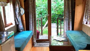Una cabaña compacta con kitchenette, dos camas individuales, una mesita y una puerta que da a una terraza exterior.