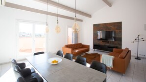 Un vaste espace de vie comprenant une grande table à manger, un canapé marron et un téléviseur à écran plat fixé au mur.