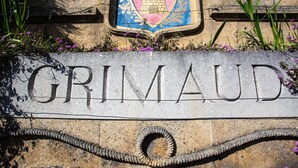 Une plaque de pierre portant le nom « GRIMAUD » et un blason.