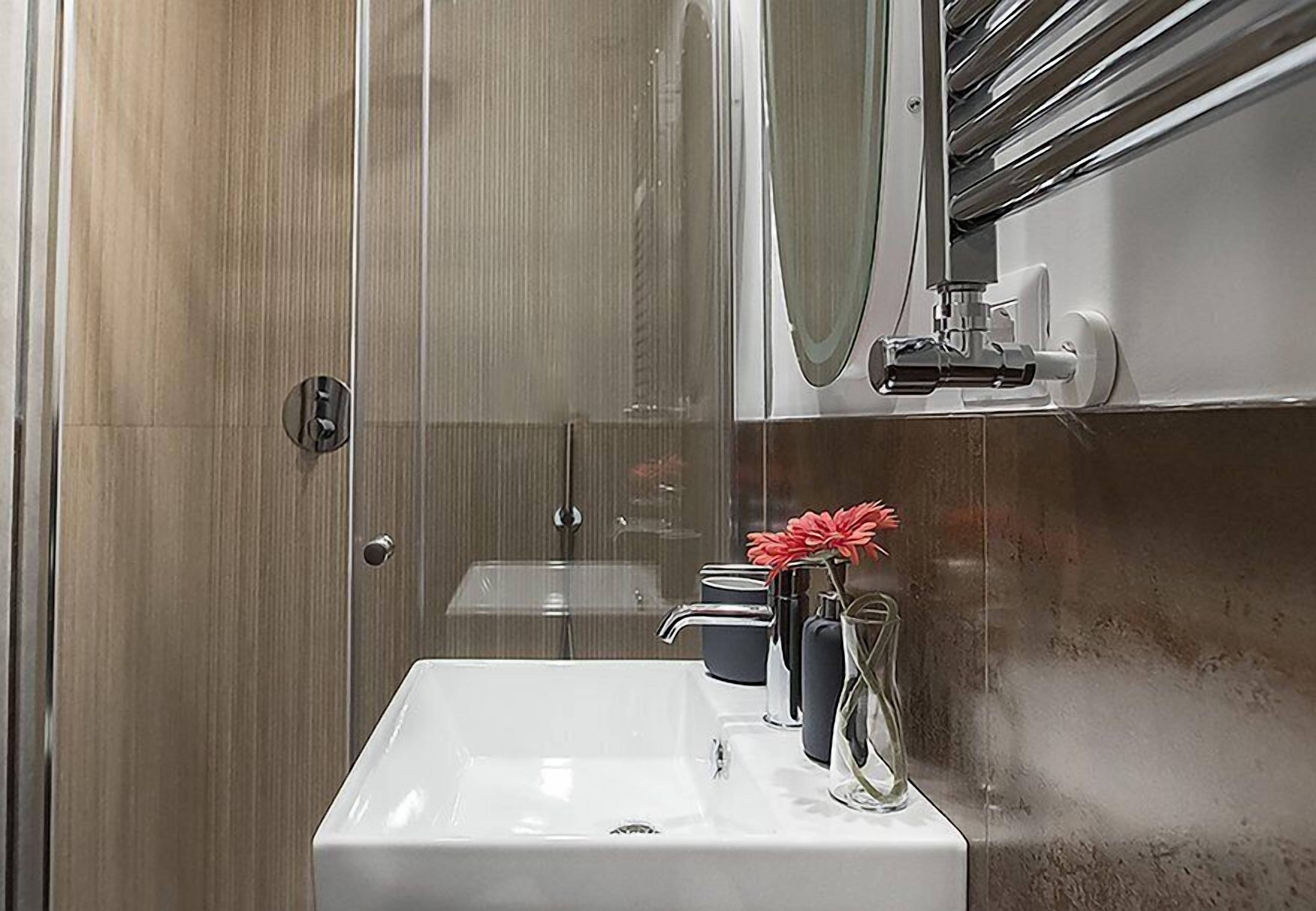A modern bathroom with a white sink, a mirror, and a shower area.