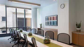 A conference room with a long table, chairs, a clock, and a plant.