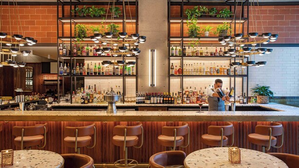 A bar area with multiple shelves of liquor bottles, a bartender, and several bar stools. - Element by Marriott Philadelphia Downtown (Philadelphia)