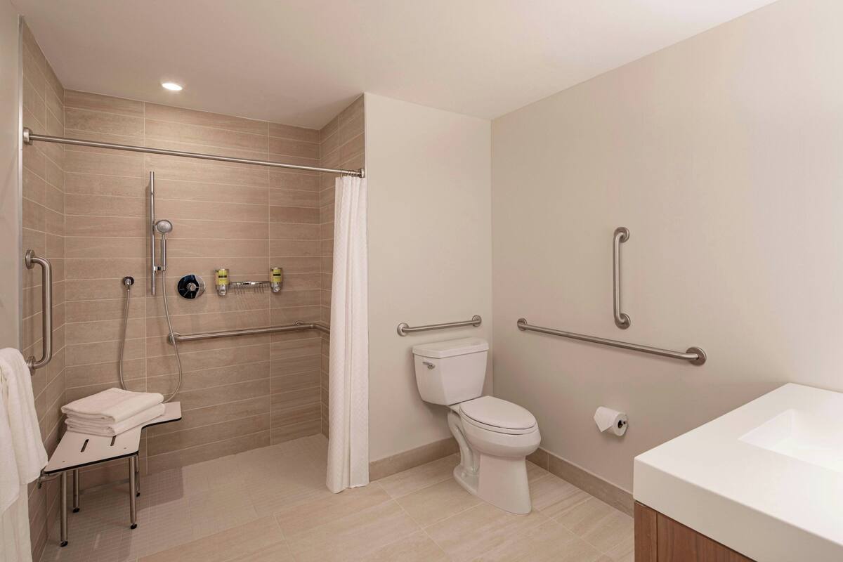 A modern bathroom with a shower, toilet, and sink, equipped with handrails and grab bars for accessibility.