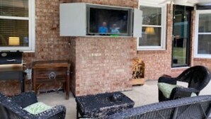 Eine Terrassenausstattung mit Backsteinmauer, einem an der Wand befestigten Fernseher und Gartenmöbeln.