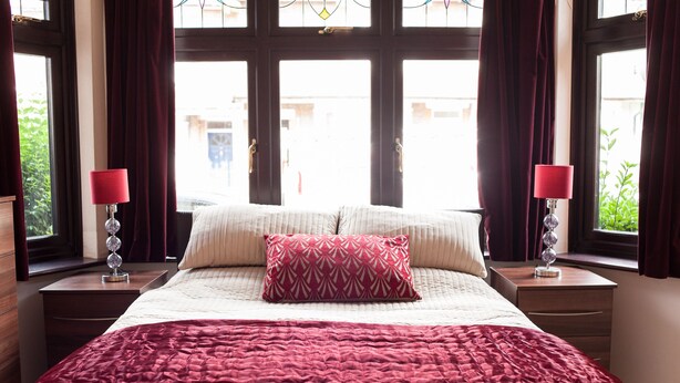 Ein ordentlich bezogenes Bett mit einem roten und weißen Kissenmuster, einer roten Decke und zwei Nachttischlampen mit roten Lampenschirmen.