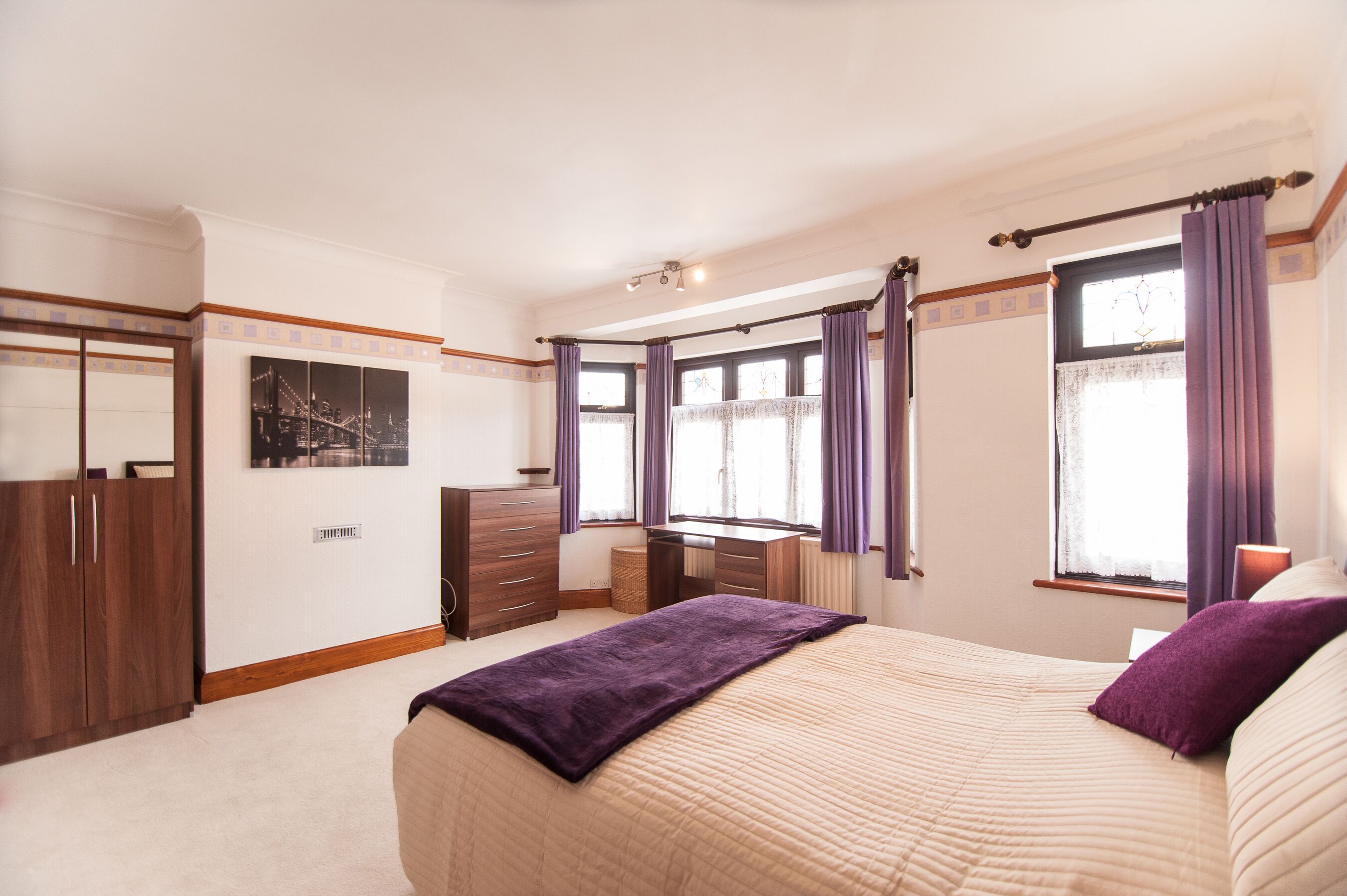 Un dormitorio con cama, cómoda, armario y ventana con cortinas.