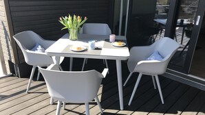 A table with chairs on a wooden deck, a vase with flowers, and a plate with food.
