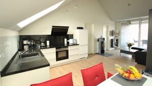 A modern kitchen with a black countertop, white cabinets, and a dining area with red chairs.