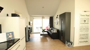 A modern living room with a black sofa, a coffee table, and a kitchen area with a refrigerator and a microwave.