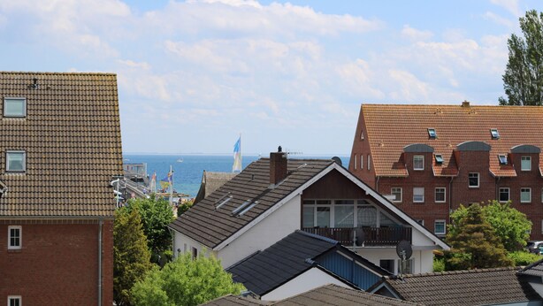 A coastal residential area with a mix of brick and tiled buildings, a visible flag, and a clear view of the sea in the background.