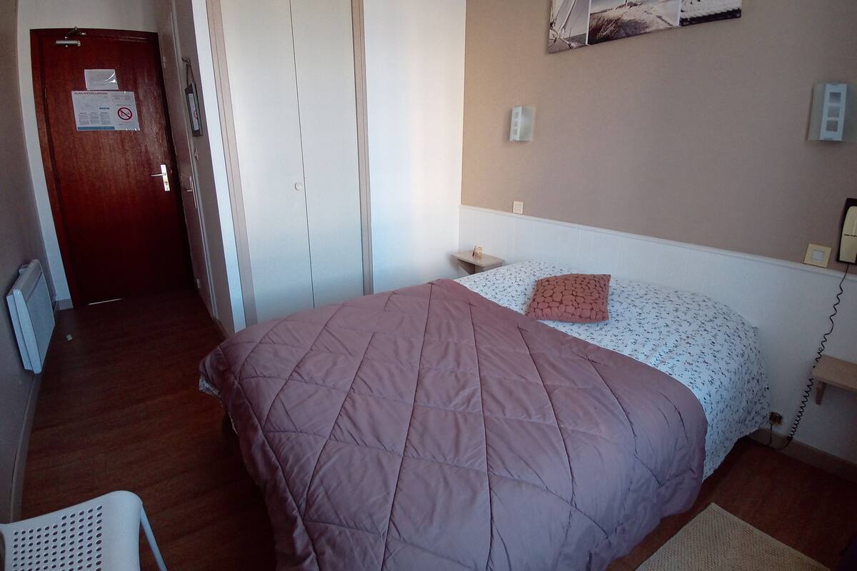Un dormitorio con cama, mesita de noche, silla y una puerta con un aviso.