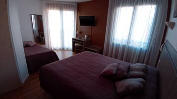 Ein Hotelzimmer mit zwei Betten, einem Schreibtisch, einem Sessel, einem Fernseher und großen Fenstern mit Vorhängen.