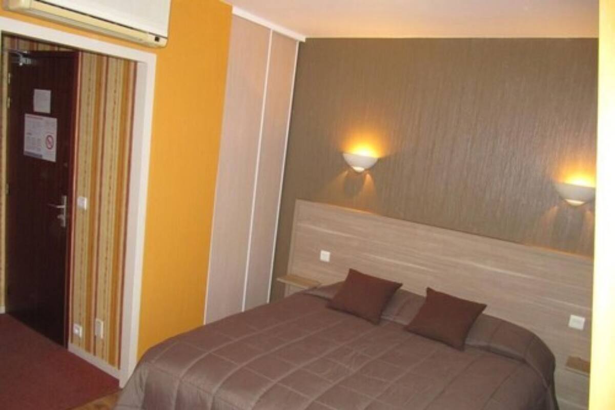 Una habitación de hotel con una cama, dos lámparas de pared, un cabecero de madera y una puerta con estampado a rayas.