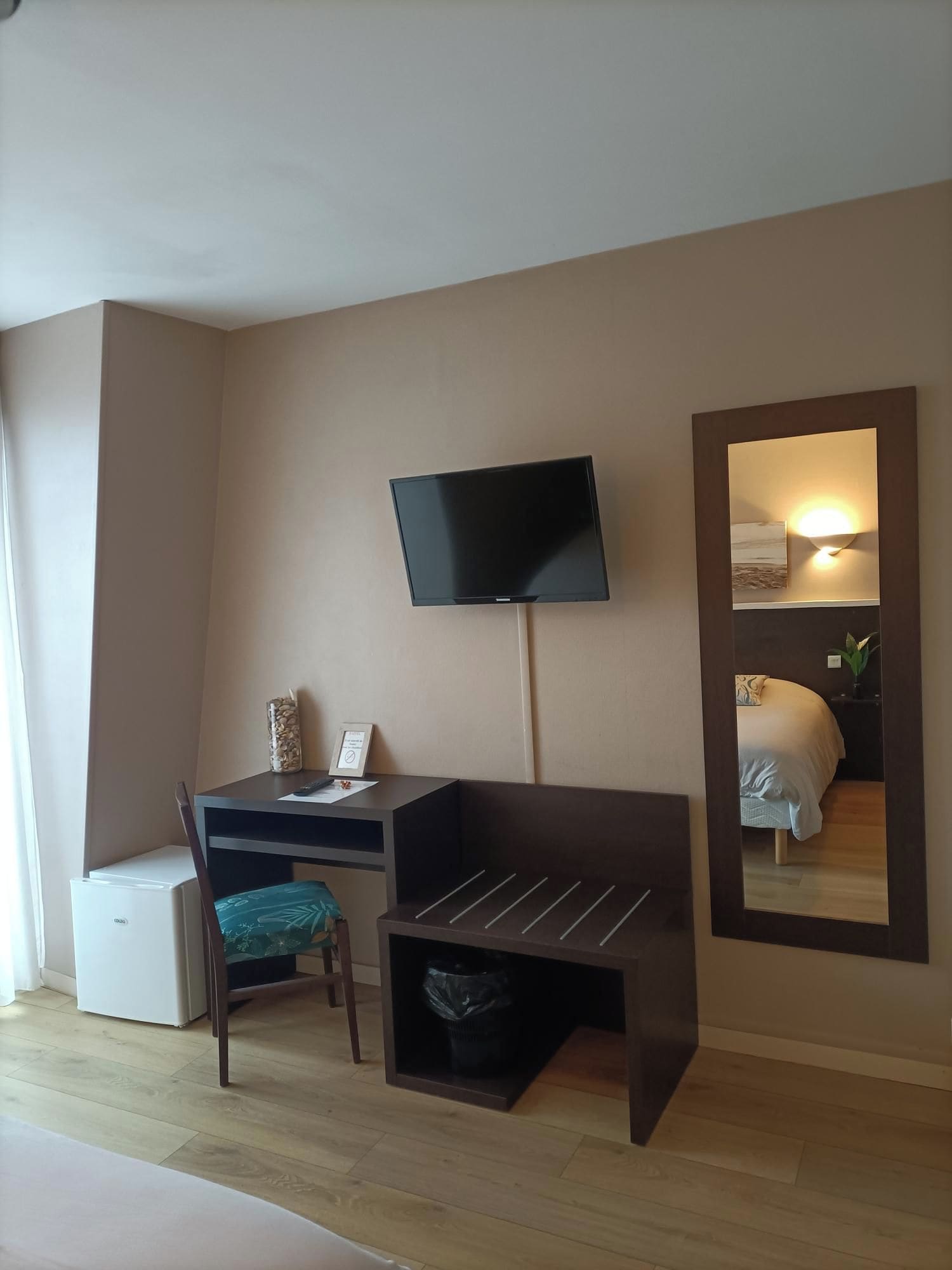 A hotel room with a desk, chair, television, and a mirror.