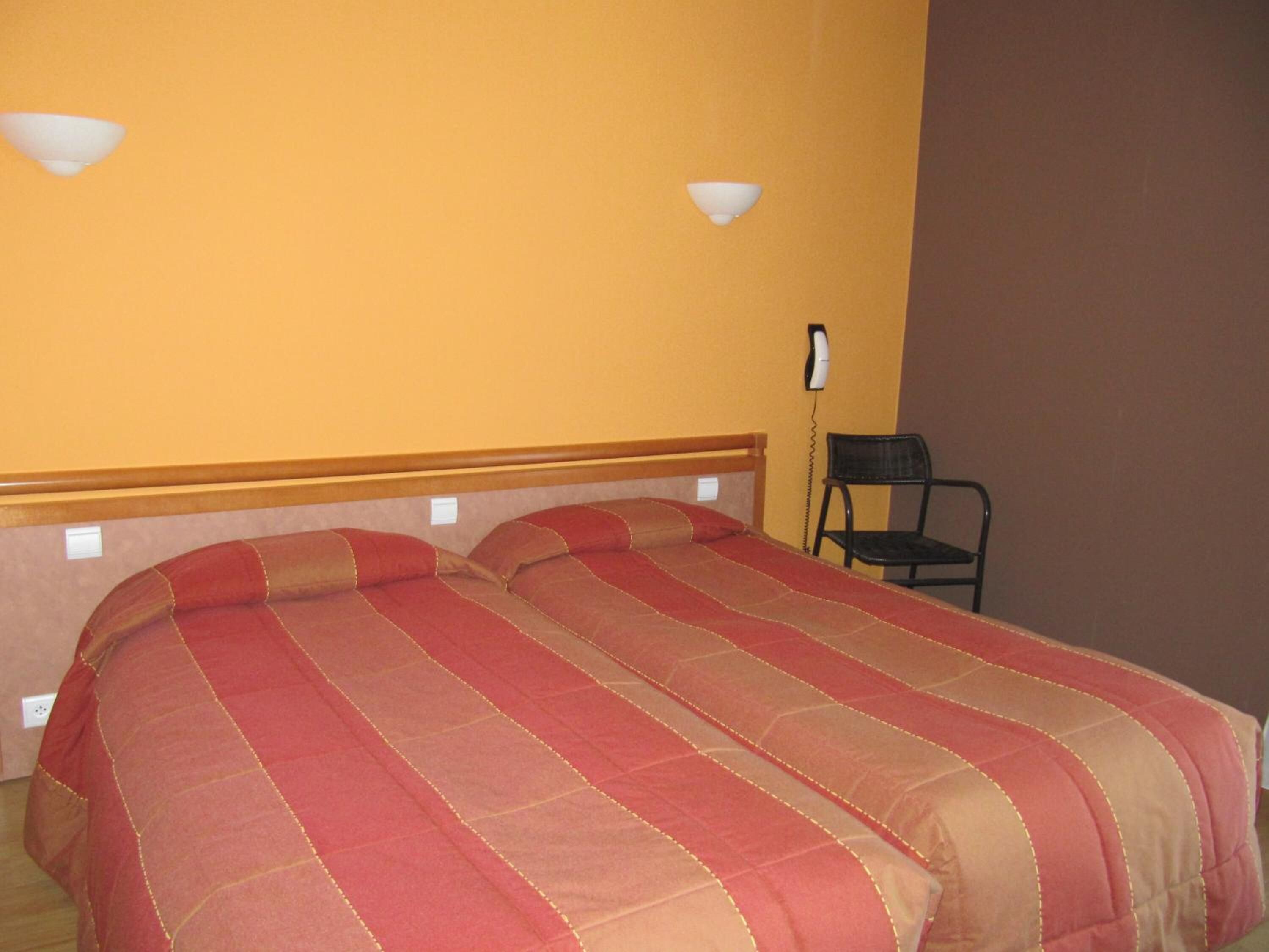 Una habitación con dos camas, una silla y un teléfono en la pared.