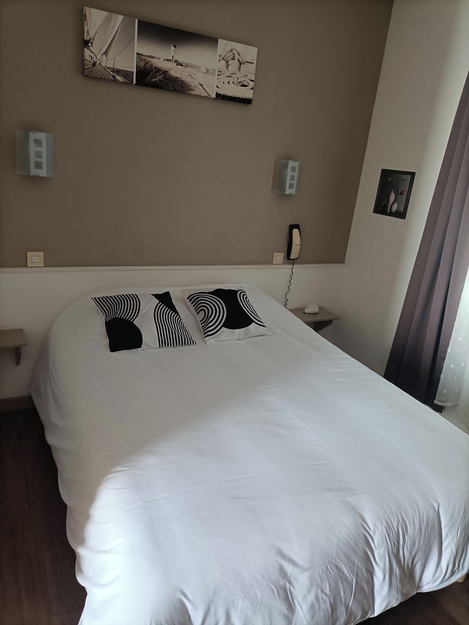 Une chambre d’hôtel avec un grand lit, une table de chevet, un téléphone et un tableau accroché au mur.