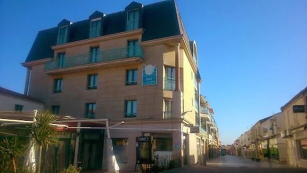 Un hotel de varios pisos con un balcón en el segundo piso, un cartel que indica que es un hotel y un cielo azul despejado al fondo.