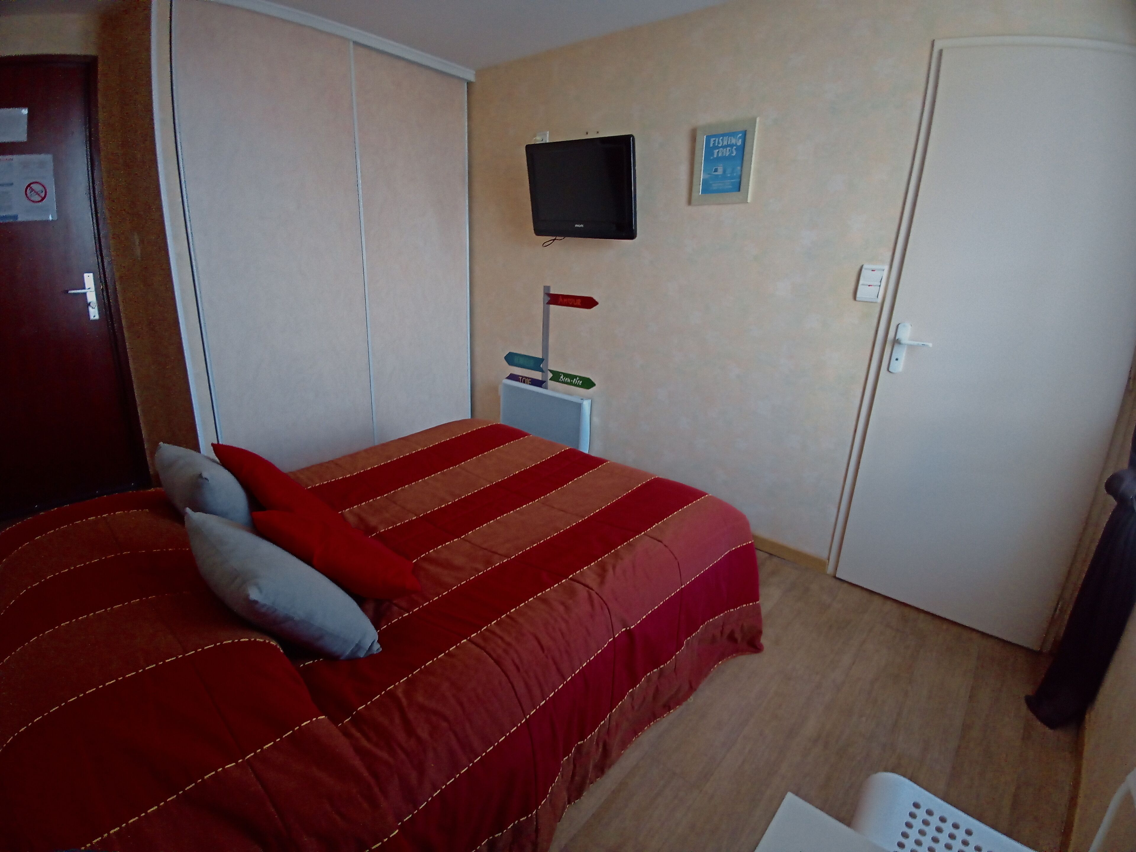 A bedroom with a bed, a TV mounted on the wall, a sign indicating a fishing trip, and a wardrobe.