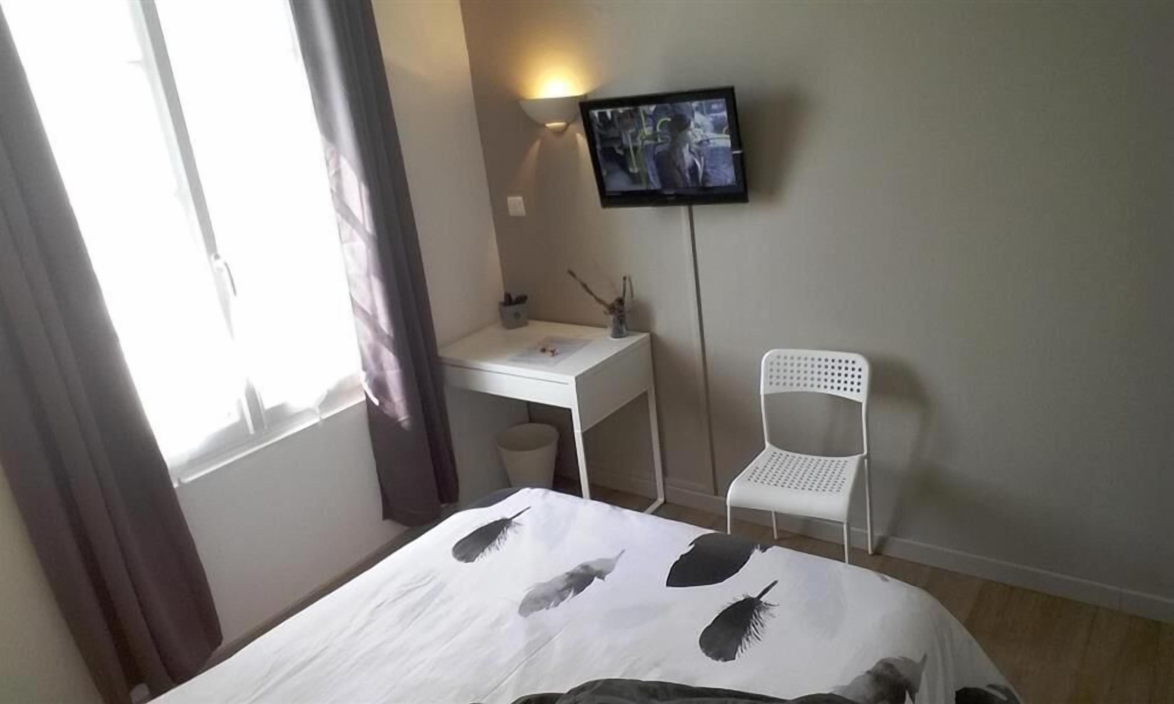A hotel room with a bed, a desk, a chair, a TV, and a window with curtains.