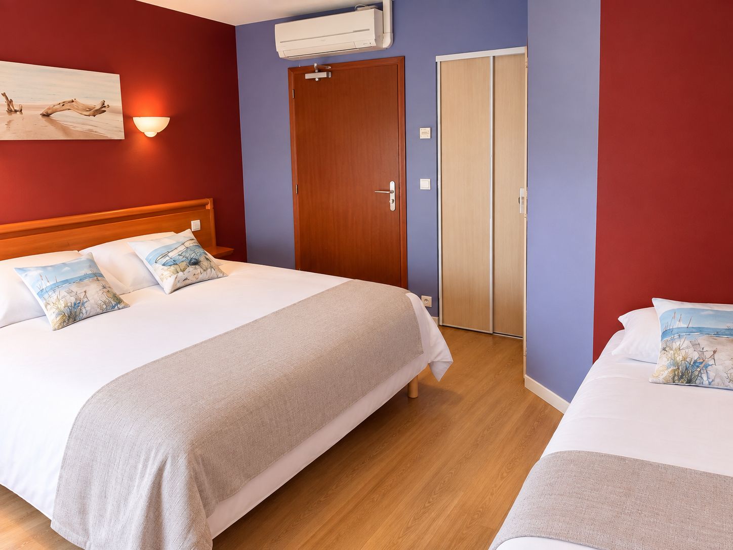 A hotel room with a bed, a nightstand, a wall-mounted air conditioner, and a door.
