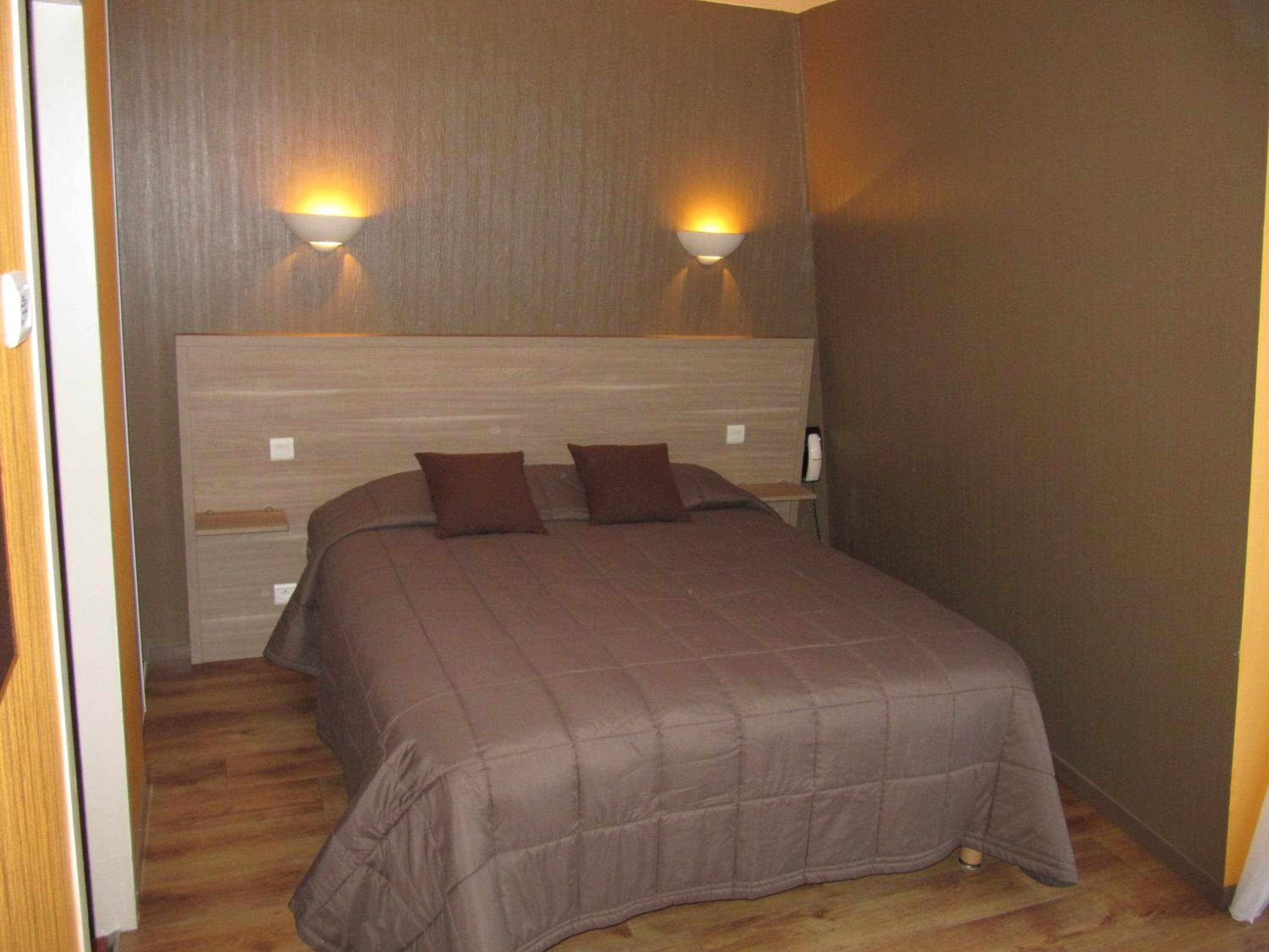 Un dormitorio con una cama grande, dos luces fijadas a la pared y un cabecero de madera.