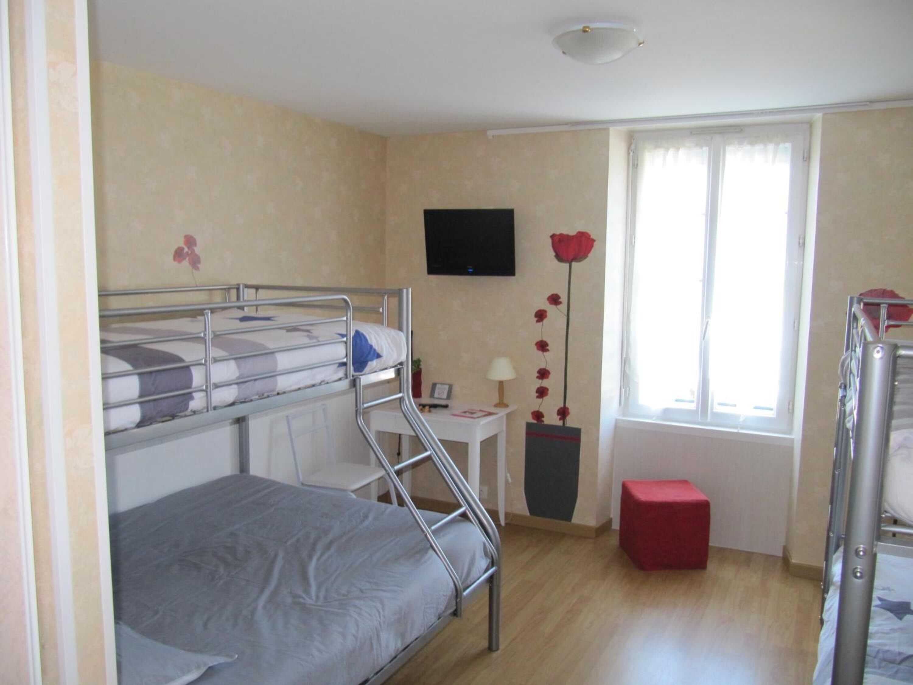 Une chambre de dortoir avec des lits superposés, un bureau, une chaise, un téléviseur fixé au mur et une fenêtre avec des rideaux.