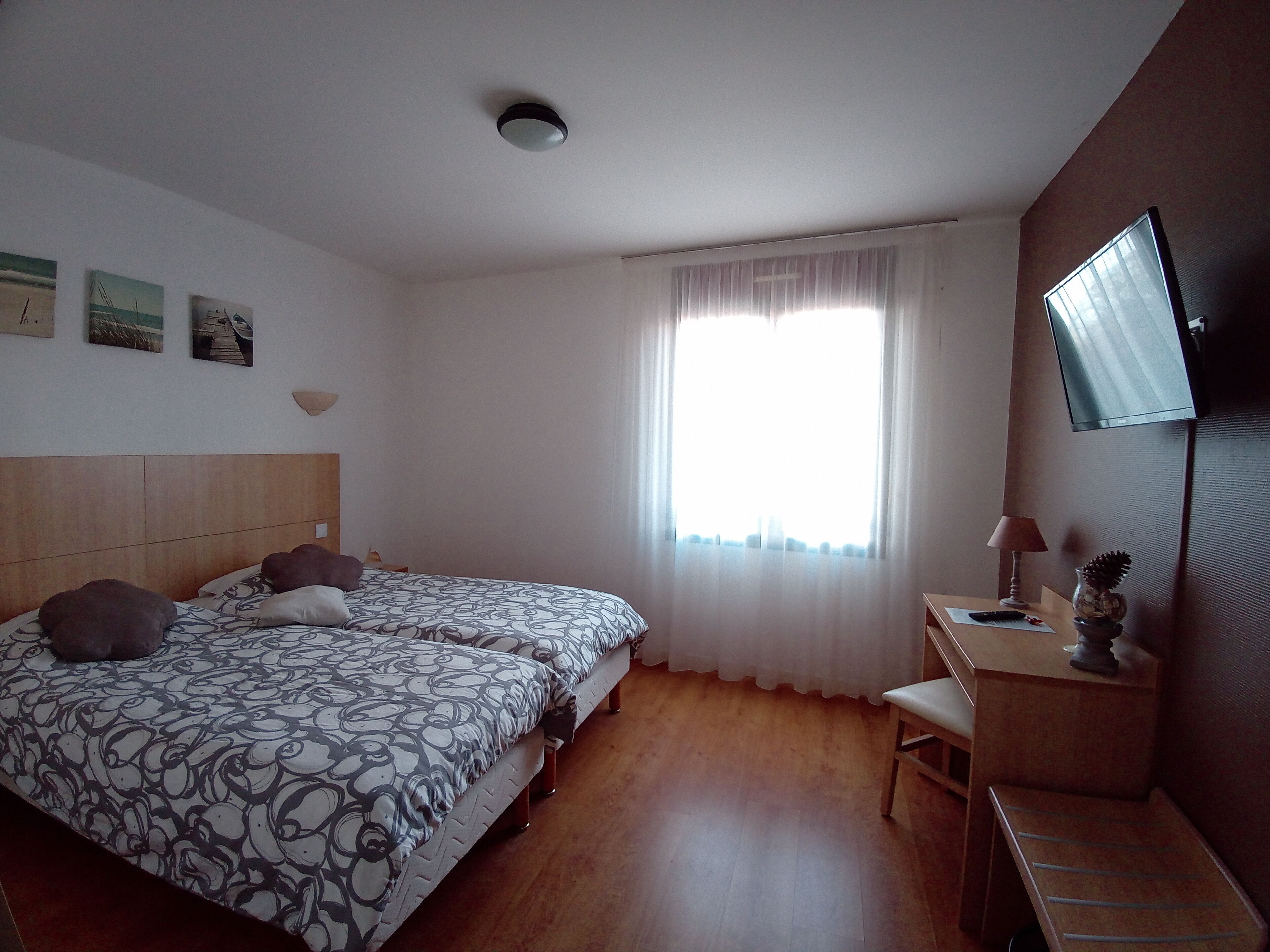 Un dormitorio con cama, escritorio, silla, televisor y ventana con cortinas.