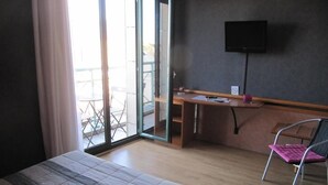 Habitación de hotel con cama, escritorio, silla, televisor y puerta corrediza al exterior.