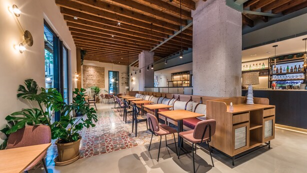 Un restaurante moderno con vigas de madera, una zona de bar y plantas en macetas.