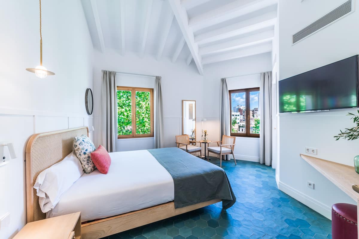 A hotel room with a bed, a desk, a chair, a TV, and large windows with curtains.