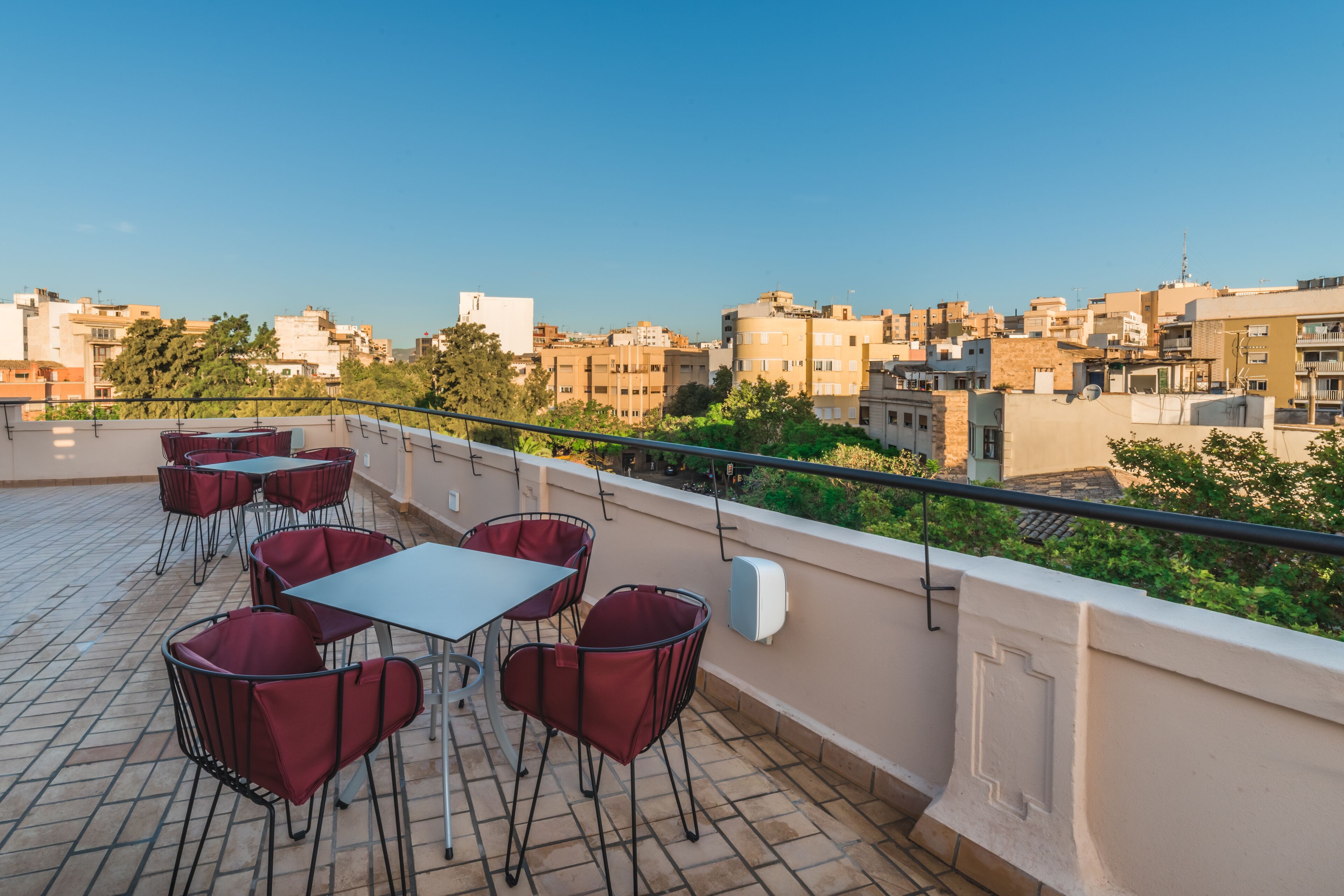 A rooftop terrace with tables and chairs, offering a view of a cityscape.