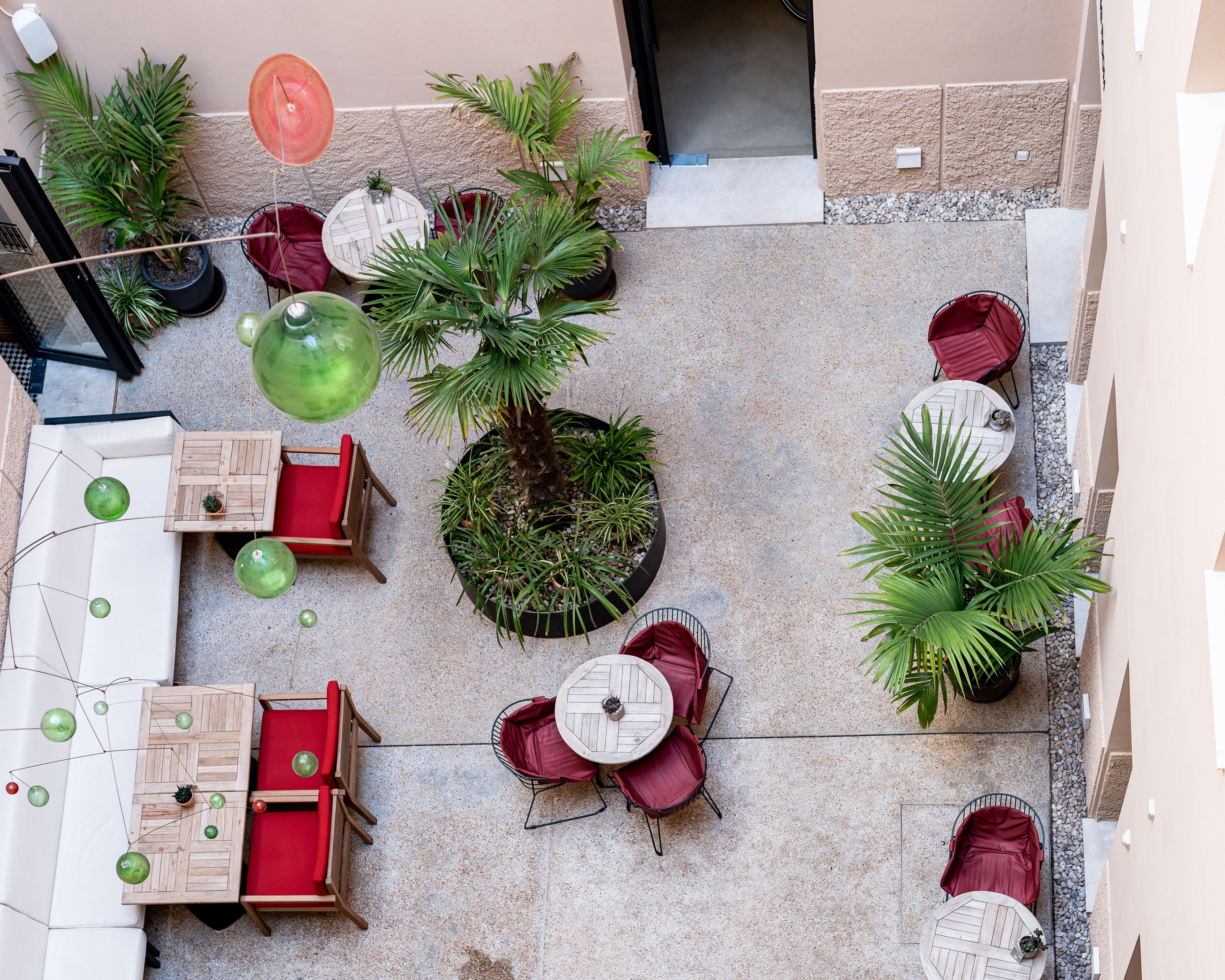 An outdoor patio area with multiple seating arrangements, including tables and chairs, surrounded by potted plants and a central tree.
