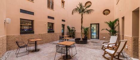 Un amplio patio con una palmera, zonas de estar y la entrada a un edificio.