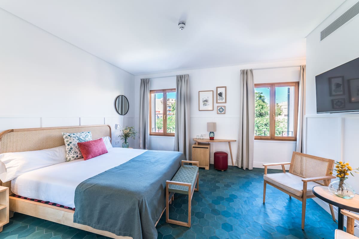 A hotel room with a large bed, a desk, a chair, and a TV.