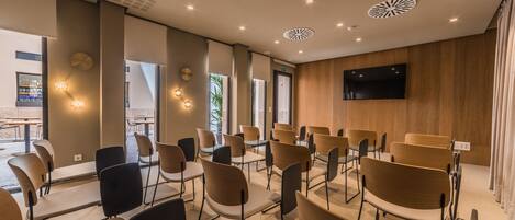 Une salle de conférence avec des rangées de chaises, un téléviseur à écran plat et des luminaires au plafond.