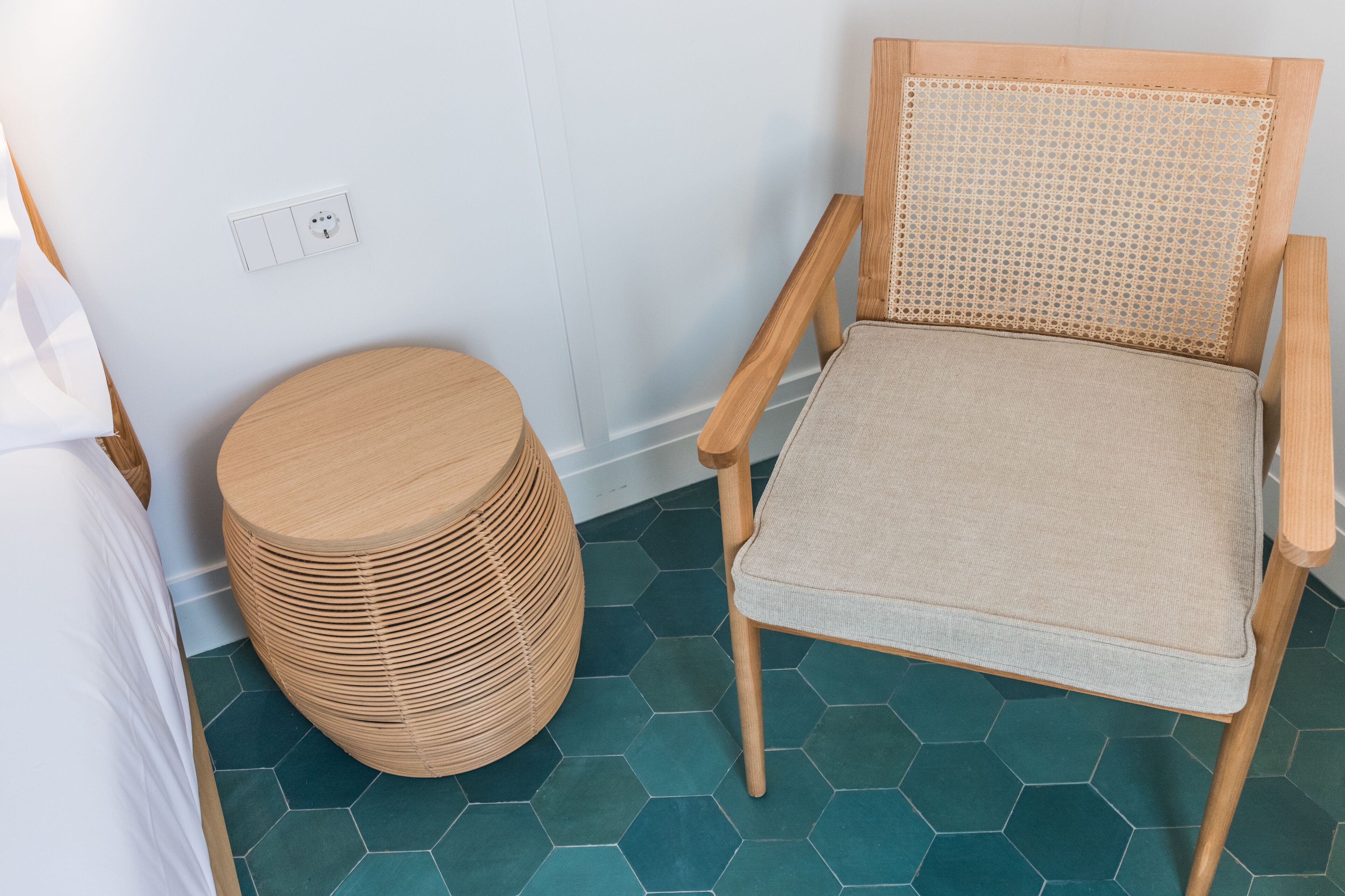 Une pièce comprenant une chaise en bois avec un dossier tressé, un tabouret rond également tressé et un sol carrelé à motifs hexagonaux.