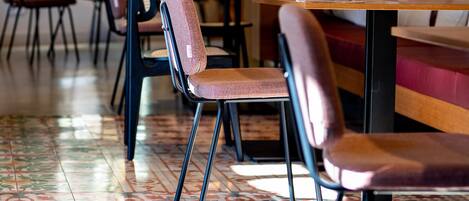 A restaurant interior with patterned floor tiles, wooden tables, and cushioned chairs.