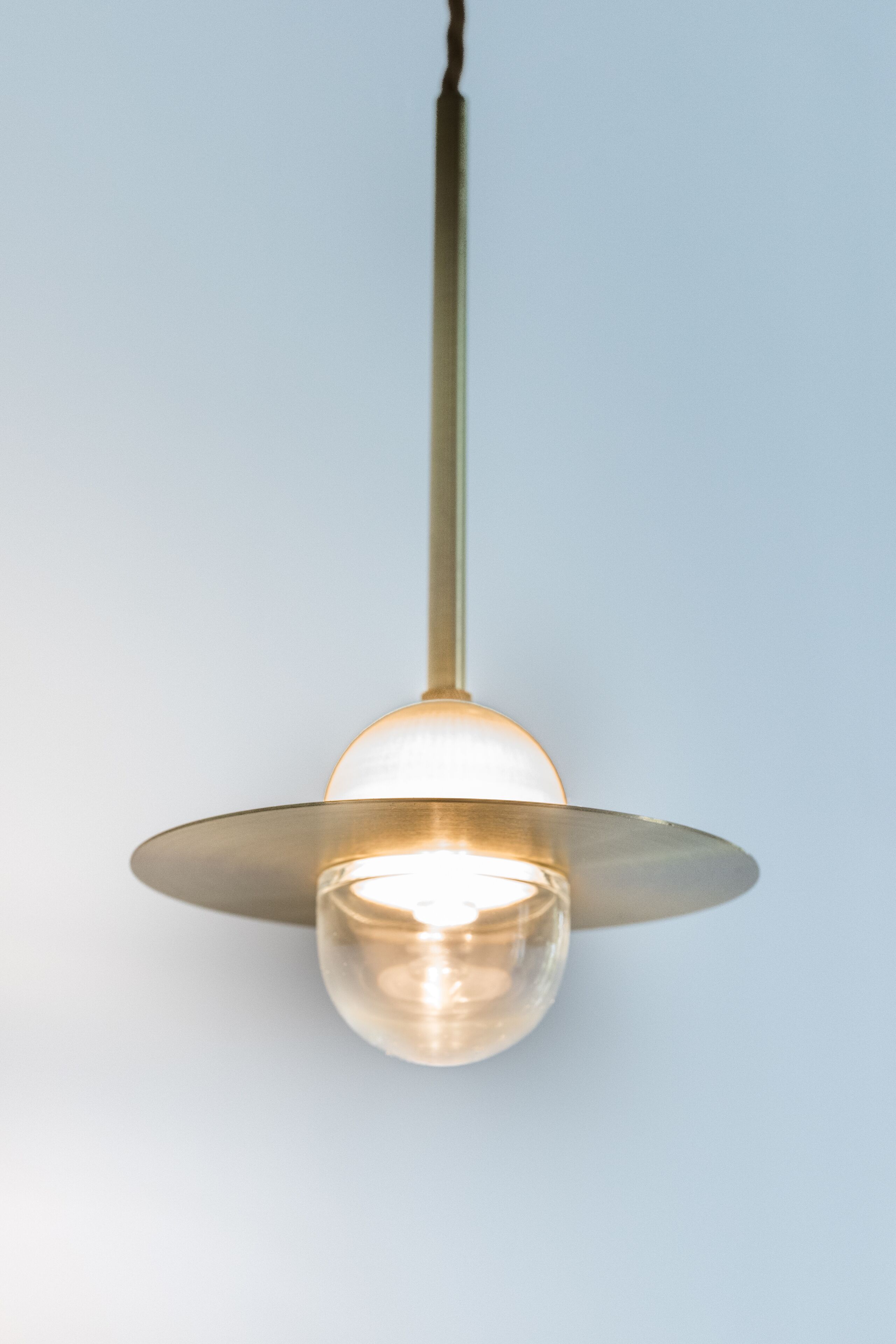 A pendant light fixture with a clear glass shade and a metallic base, hanging from a straight rod.