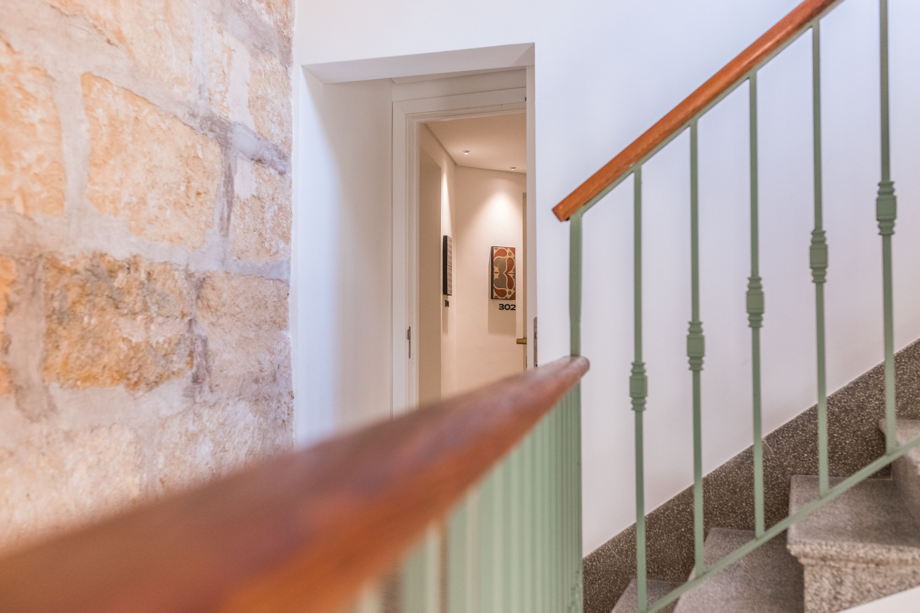 A staircase with a wooden handrail and green balusters, leading to a room with a stone wall and a door labeled "302".