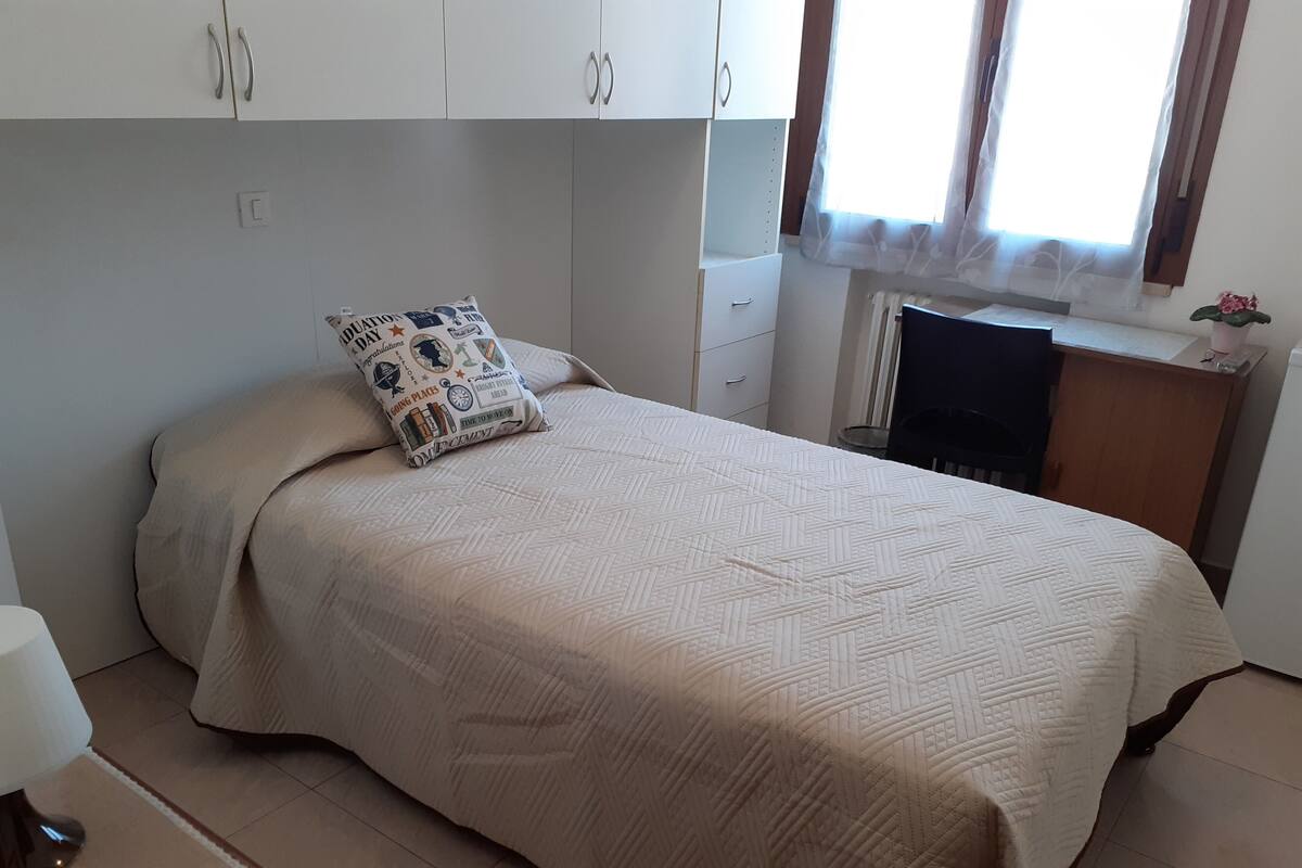 A bedroom with a bed, a bedside table, a lamp, a wardrobe, and a window with curtains.