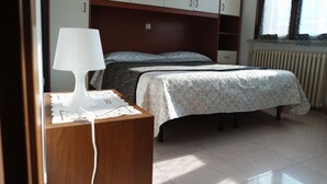 A bedroom with a bed, a bedside table with a lamp, a wardrobe, and a radiator. - Le terrazze rooms (Occhiobello)