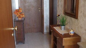 A hallway with a wooden door labeled '1', a small wooden cabinet with a potted plant, and a mirror on the wall. - Le terrazze rooms (Occhiobello)