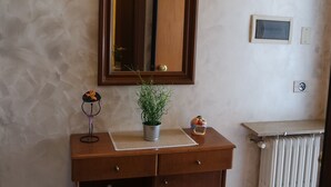 A bathroom with a wooden vanity, a mirror, a radiator, and a small shelf with decorative items. - Le terrazze rooms (Occhiobello)