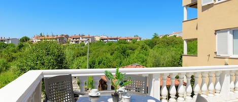 A balcony with a round table, chairs, and a potted plant.