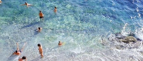 A beach with clear water and people swimming and sunbathing.