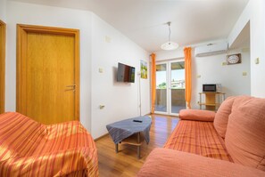 A room with a wooden door, a television mounted on the wall, a small table with a remote control, and a sofa with striped cushions. - Lovely Flat with swimming pool near beach (Vinkuran)