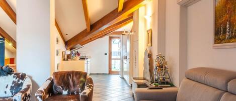 A spacious living area with a high ceiling, a fireplace, and a dining area in the background.