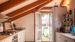 A kitchen with a gas stove, oven, and white cabinets. There's a door leading to a garden. - Casa Erica (Bologna)